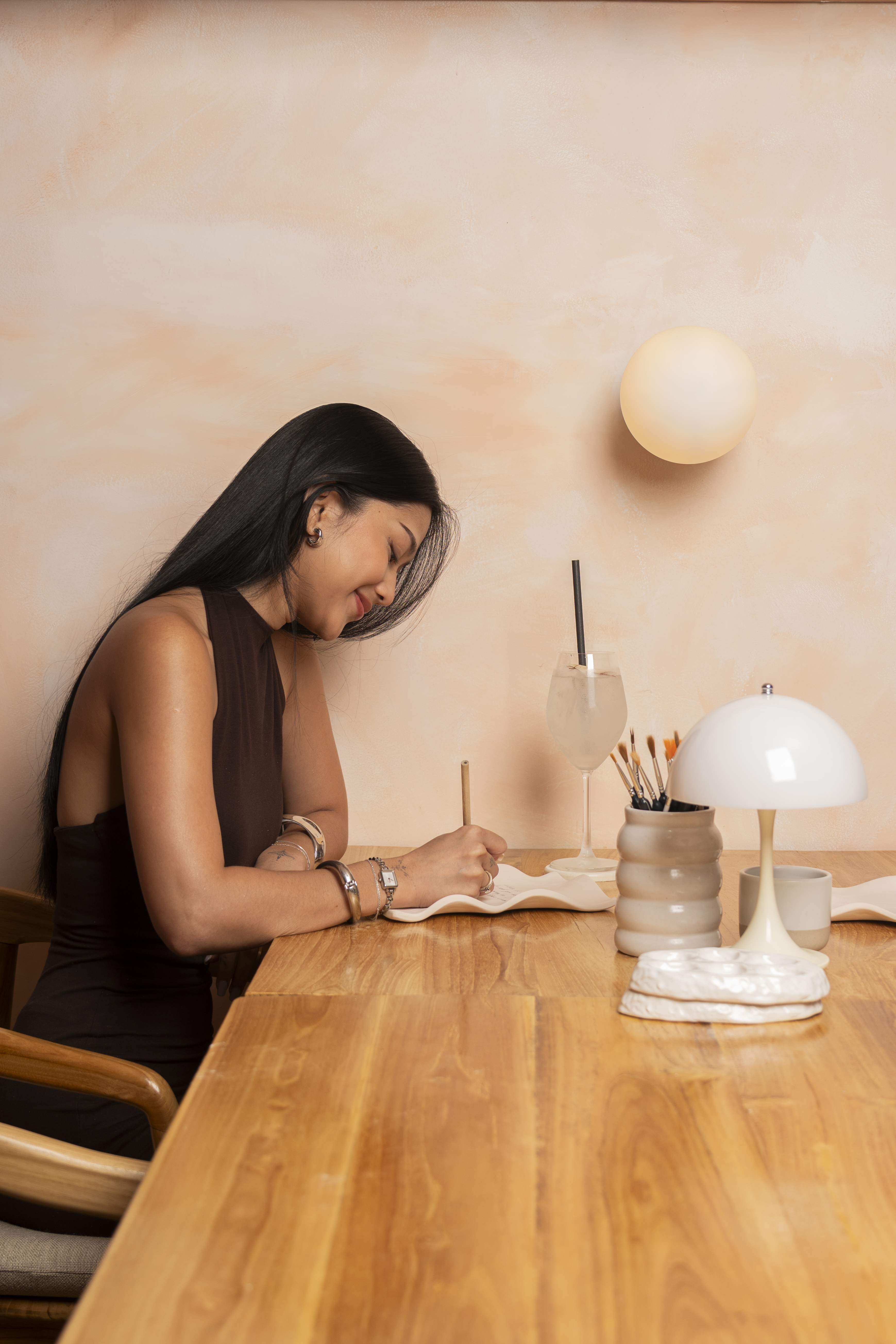 A guest painting a ceramic piece at a wooden table inside Klay Bar in Canggu, with soft lighting, brushes, and a drink nearby, capturing a quiet moment of creative focus.